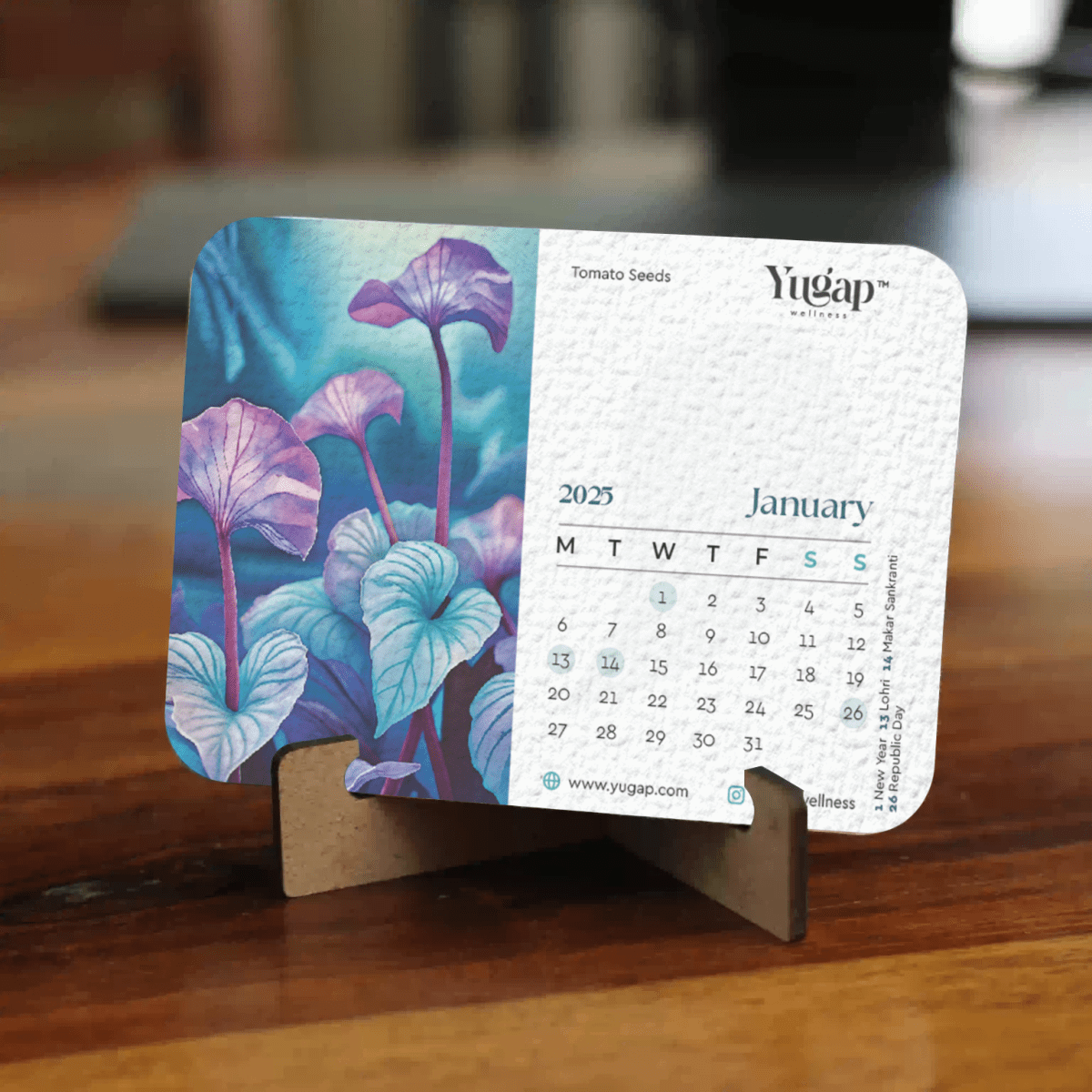 Yugap 2025 January desk calendar featuring artistic tomato seeds botanical illustration, placed on a wooden stand on table, blending nature-inspired art with functional office accessory