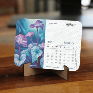 Yugap 2025 January desk calendar featuring artistic tomato seeds botanical illustration, placed on a wooden stand on table, blending nature-inspired art with functional office accessory