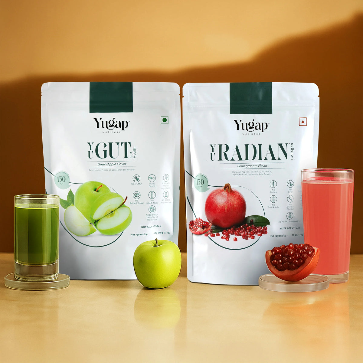 Two Yugap pouch drinks—YGute apple flavor and YRadiant pomegranate flavor—displayed with fresh green apple, pomegranate arils, and poured glasses on wooden surface, highlighting a refreshing wellness combo