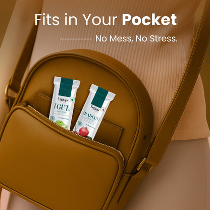 Two Yugap YGute apple and YRadiant pomegranate sachets tucked into a brown crossbody bag pocket, illustrating portable, on-the-go probiotic and skin wellness supplements