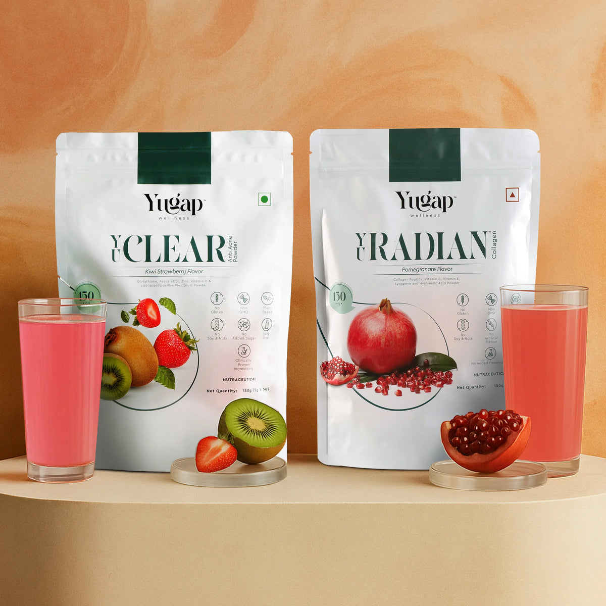 Two Yugap pouches—Yuclear kiwi strawberry flavor and Yuradian pomegranate flavor—displayed with fresh kiwi, strawberry, pomegranate arils, and poured glasses on beige surface against warm background, highlighting vibrant wellness drinks